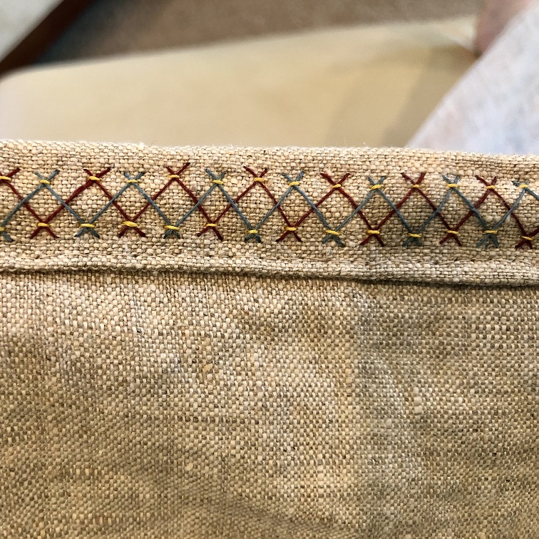 A piece of natural linen fabric with blue, red, and yellow herringbone stitch embroidery