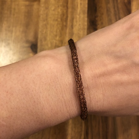 A woman's wrist wearing a woven copper wire bracelet