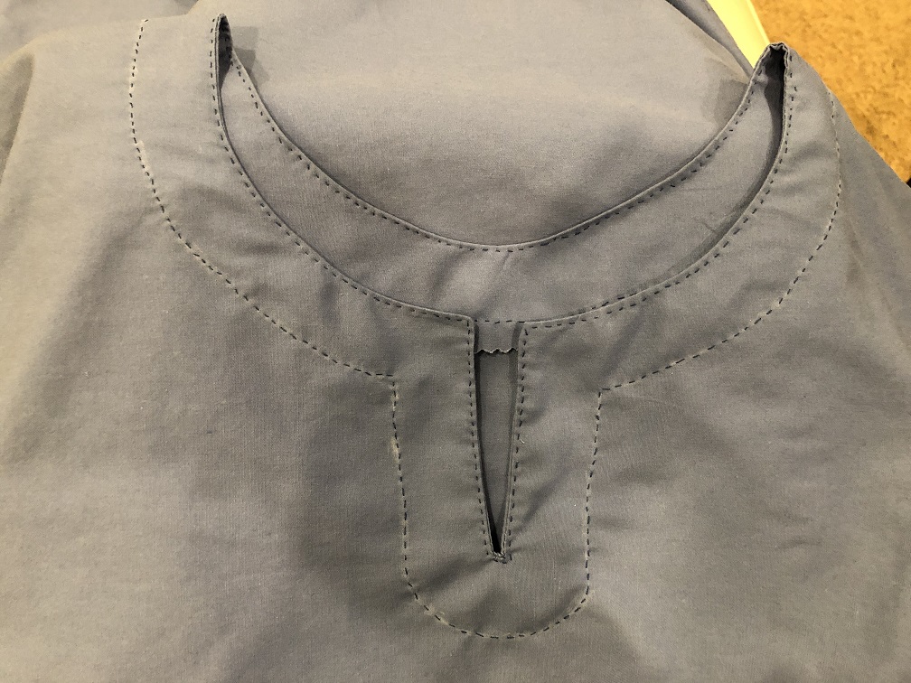 A keyhole neck on a blue viking style underdress with dark blue thread stitched around the border of the neck and neck facing