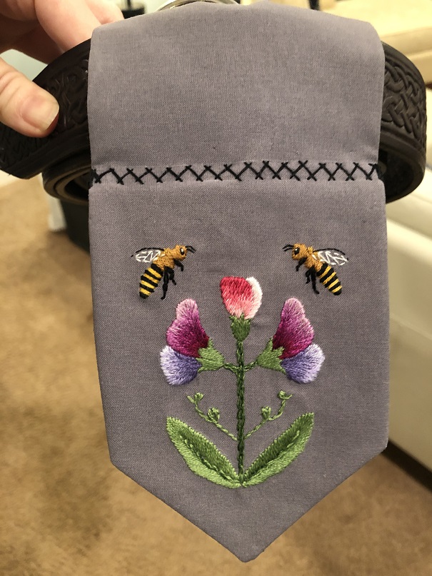 A photo of the grey cloth embroidered with bees and sweet peas attached to a belt