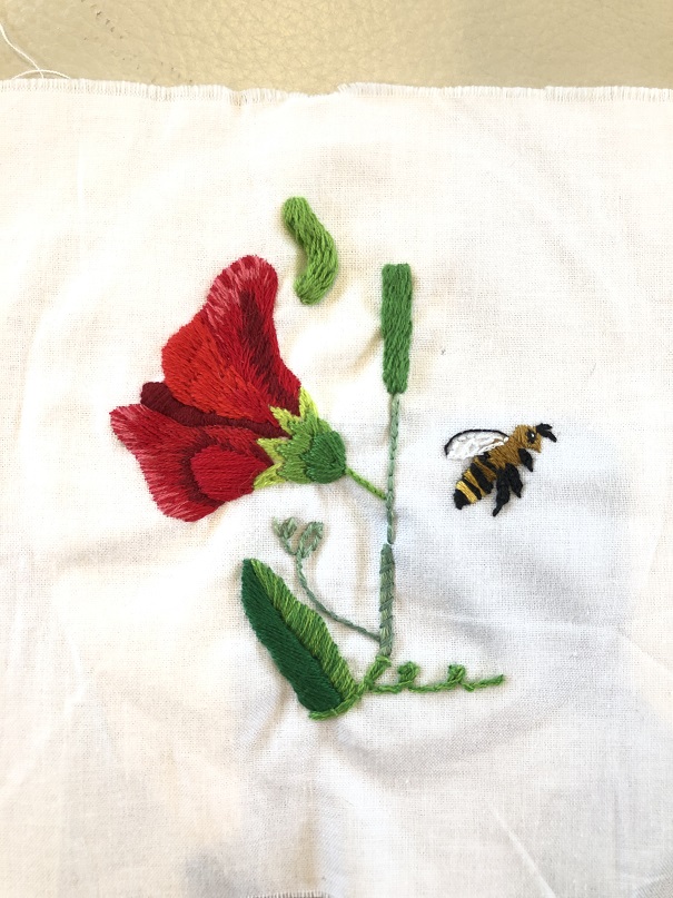 A white cloth with a red flower embroidered on it, as well as a bee and several green stems