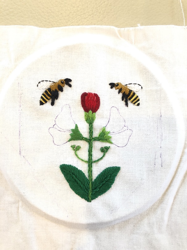 A white cloth with two bees embroidered on it, as well as two sweet pea flowers and their leaves