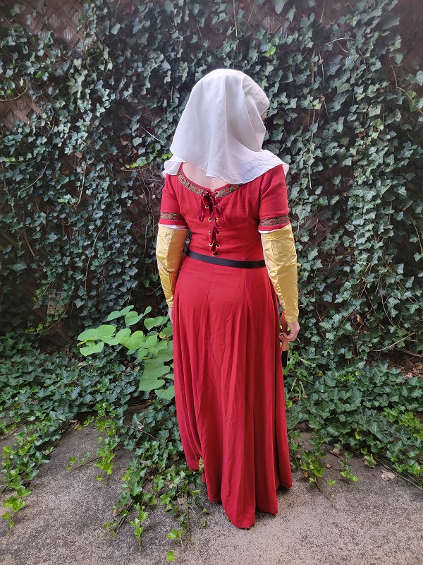 A woman facing away from the camera wearing a red dress with gold silk sleeves, a black belt, and a white veil