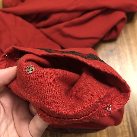 A close up of the inside of a red dress sleeve showing a silver eye fastener and a silver snap fastener sewn to the sleeve