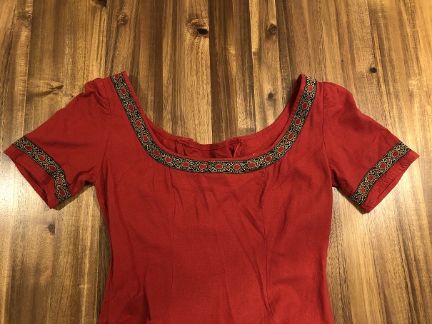 A red short sleeved linen dress lying on a wood table, shown from the waist up