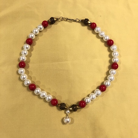 A choker length necklace made up of pearls, red beads, and brass beads on a gold silk background