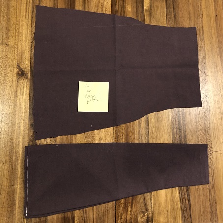 Two pieces of purple cotton on a wood table. One is laid flat with a post-it note that reads sleeve pattern, the second is a sewn sleeve