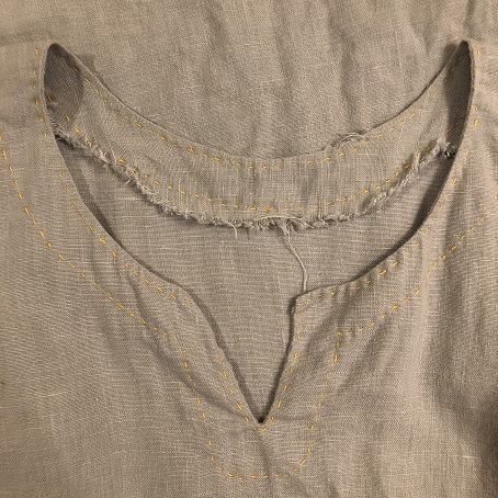 A photo of the collar on a light grey tunic with a frayed neck facing due to washing