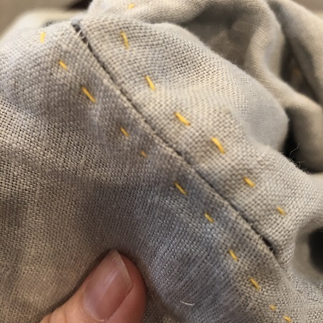 A close up photo of stretched threads in a sleeve seam on a light grey tunic