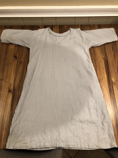 A light grey linen tunic spread out on a wooden table