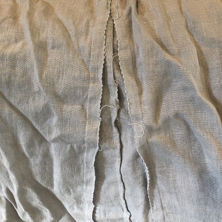 A photo of untreated seams fraying on a grey linen tunic