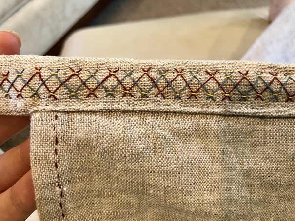 A piece of natural linen fabric with blue, red, and yellow herringbone stitch embroidery