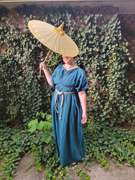 A woman wearing a teal chiton with a bright yellow palla wrapped around her in a Roman style