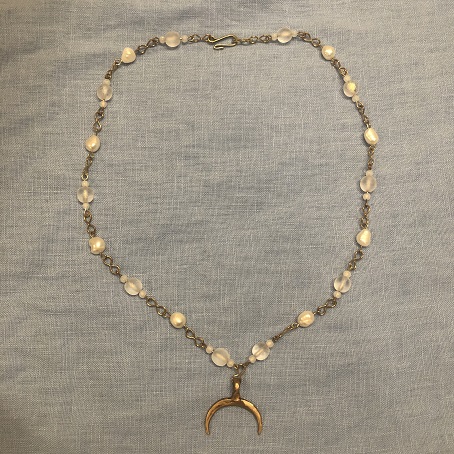 A chain style necklace with alternating pearls and clear beads, with a half moon shaped bronze pendant