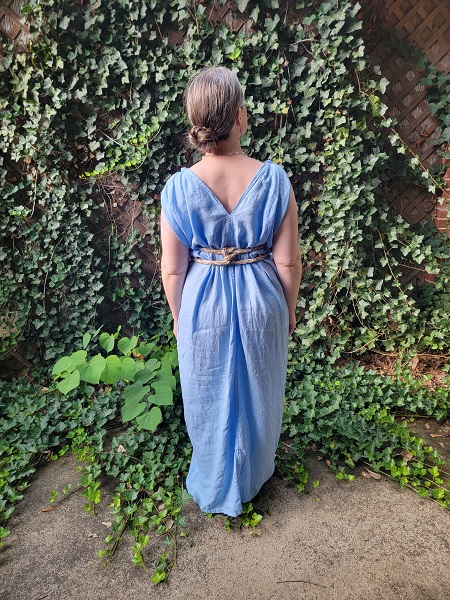 A woman wearing a light blue sleeveless dress, facing away from the camera. Her hair is in a bun, and the neckline of the back makes a V.