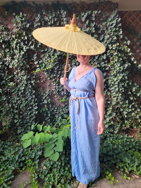 A woman wearing a light blue sleeveless V-neck tunic dress, belted at the bust and waist