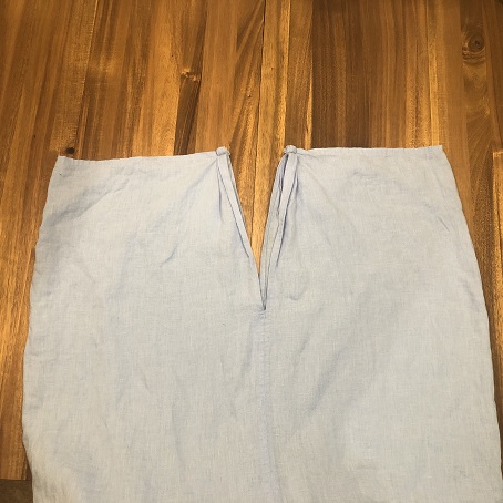 a piece of blue fabric on a wood table that is straight at the top with seams in the center sewn lower, making a V shape