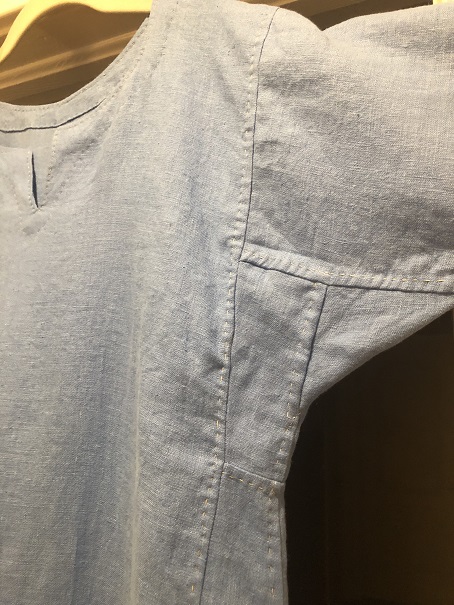 The outside of a blue Viking dress featuring the underarm gusset and side panels, with natural linen stitching visible along the seams