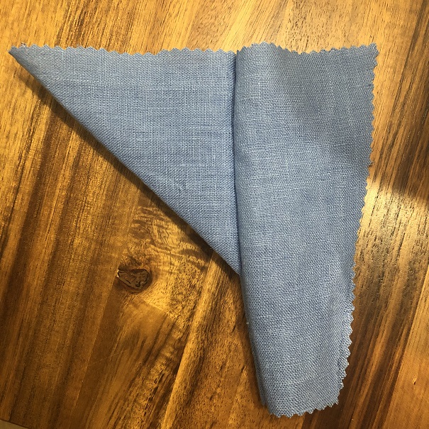 A photo of the outward-facing side of a blue fabric square, folded in half to make a triangle, sewn to a trapezoidal side panel