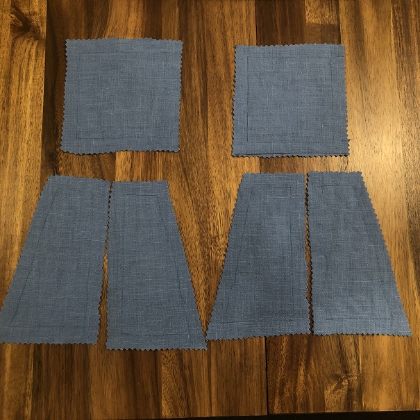 Six pieces of blue fabric ready to get sewn together. There are two square pieces and four trapezoids. There is a line drawn inside the edge of each piece a half inch from the edge.