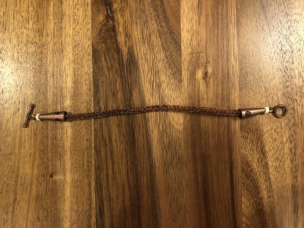 A finished copper woven wire bracelet on a wooden table