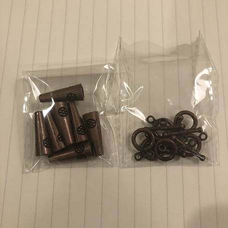 Two small clear bags of copper bead fittings, one bag is of cone end caps and the other bag is circle clasps