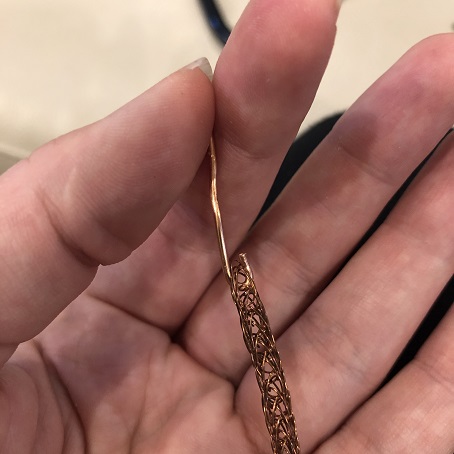 A piece of thick wire with a small hook at one end. The hook is attached to the end of some woven copper wire