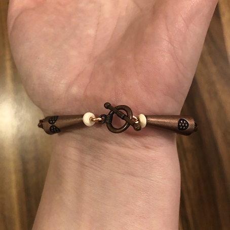 A photo of the inside of someone's wrist as they are wearing a bracelet of woven copper wire fastened with a cirle clasp